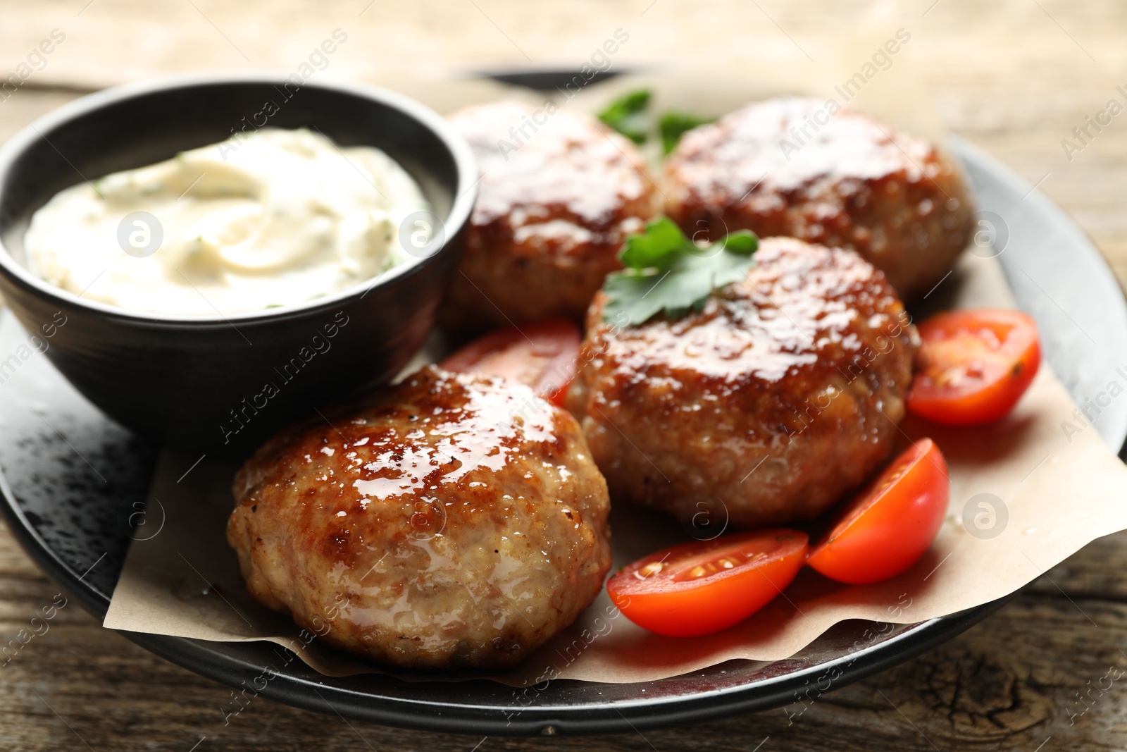 Photo of Delicious patties, parsley, tomatoes and sauce on wooden table, closeup