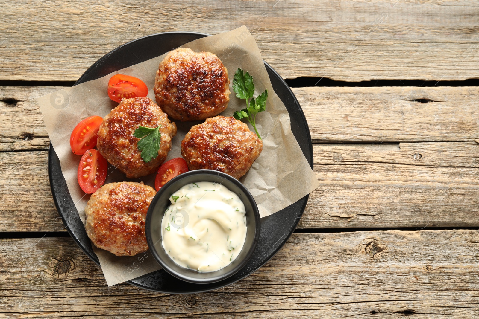 Photo of Delicious patties, parsley, tomatoes and sauce on wooden table, top view. Space for text