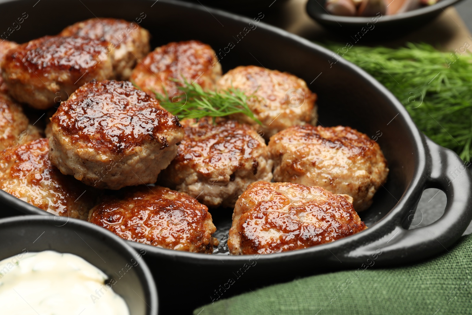 Photo of Delicious patties in baking dish, dill and sauce on table, closeup