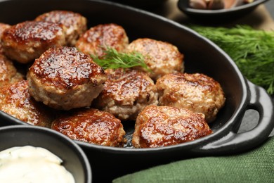 Photo of Delicious patties in baking dish, dill and sauce on table, closeup