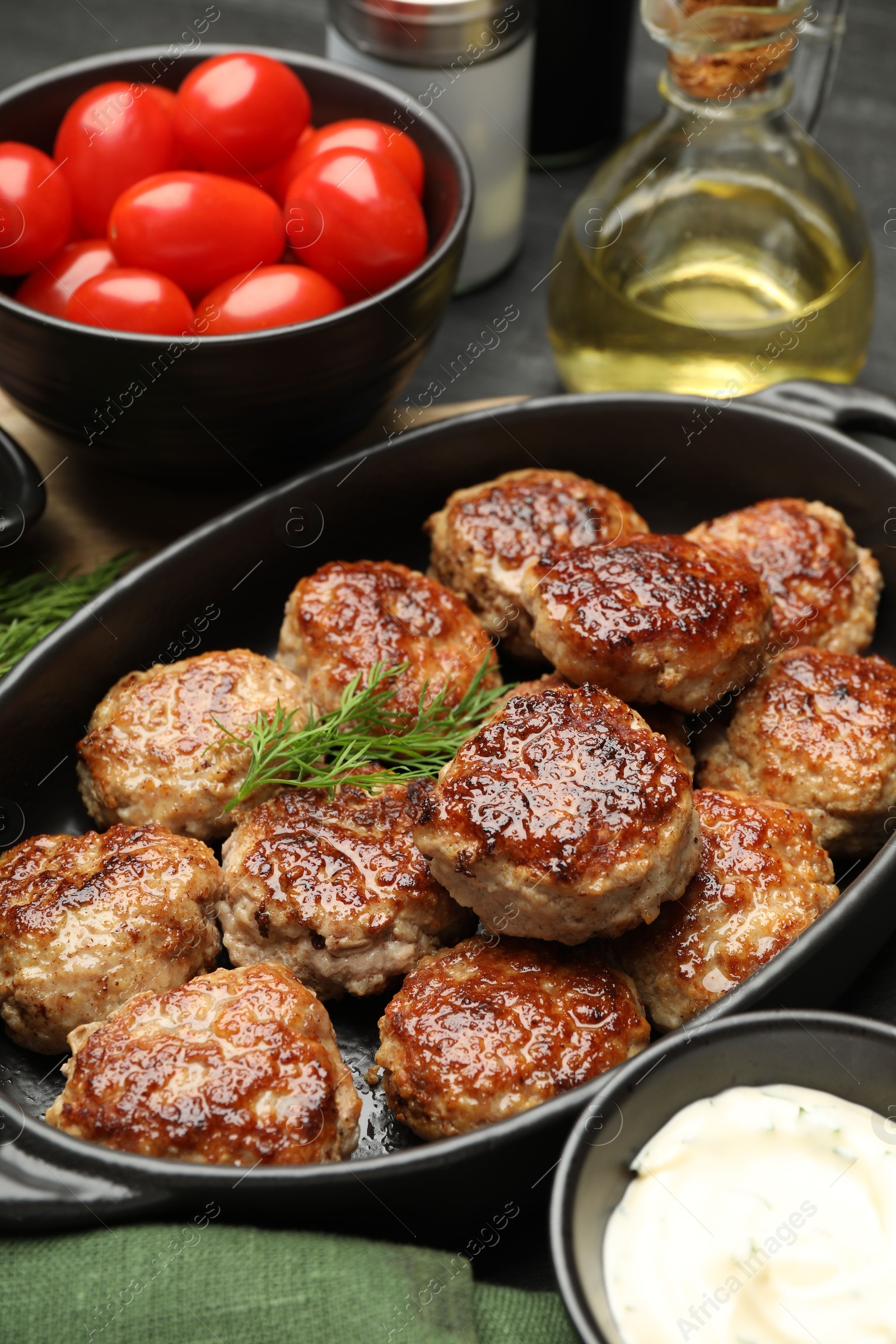 Photo of Delicious patties in baking dish, spices and tomatoes on table, closeup