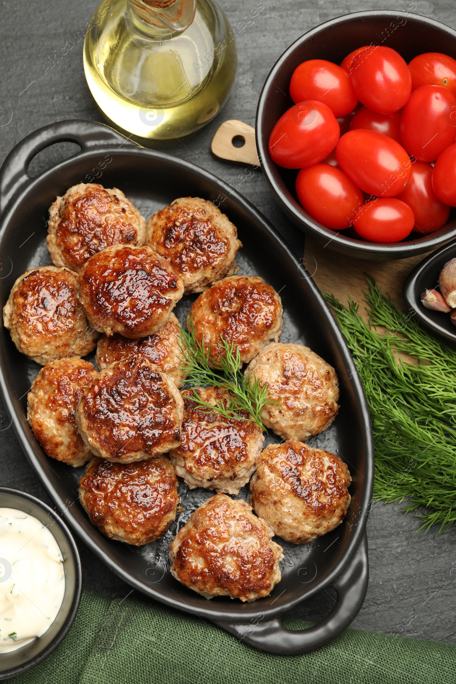 Photo of Delicious patties in baking dish, spices and tomatoes on black table, flat lay