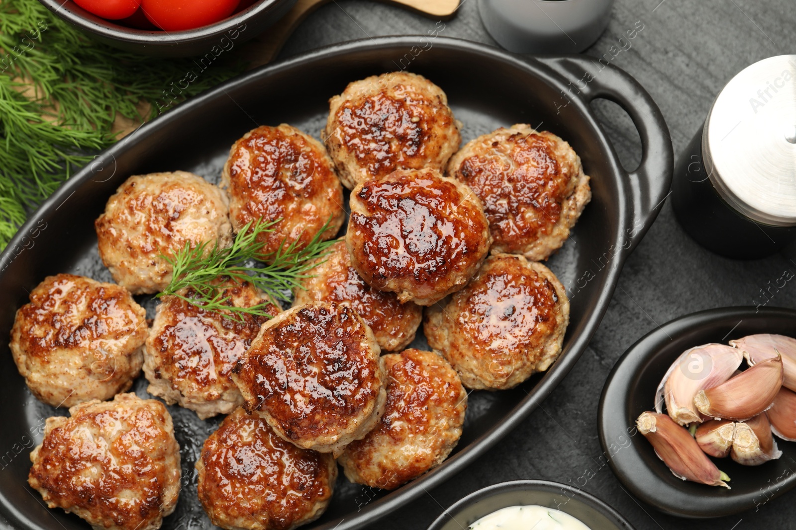 Photo of Delicious patties in baking dish and spices on black table, flat lay