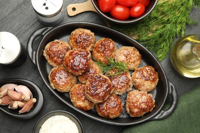 Photo of Delicious patties in baking dish, spices and tomatoes on black table, flat lay