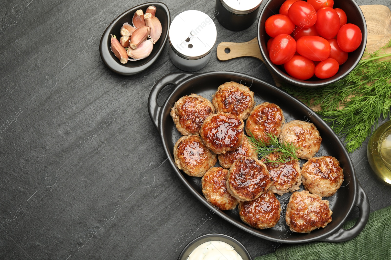 Photo of Delicious patties in baking dish, spices and tomatoes on black table, flat lay. Space for text