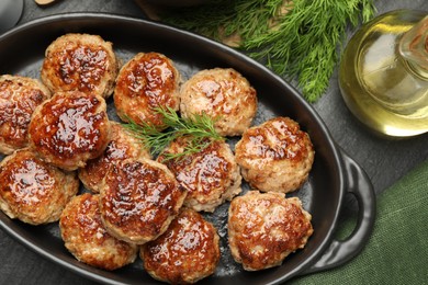 Photo of Delicious patties in baking dish, dill and oil on black table, flat lay