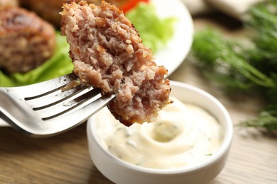 Photo of Dipping delicious patty into sauce at wooden table, closeup