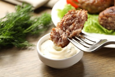 Photo of Dipping delicious patty into sauce at wooden table, closeup