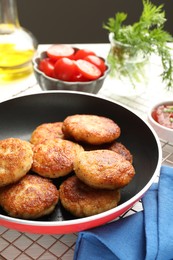 Photo of Delicious patties in frying pan, tomatoes, dill and ketchup on table, closeup