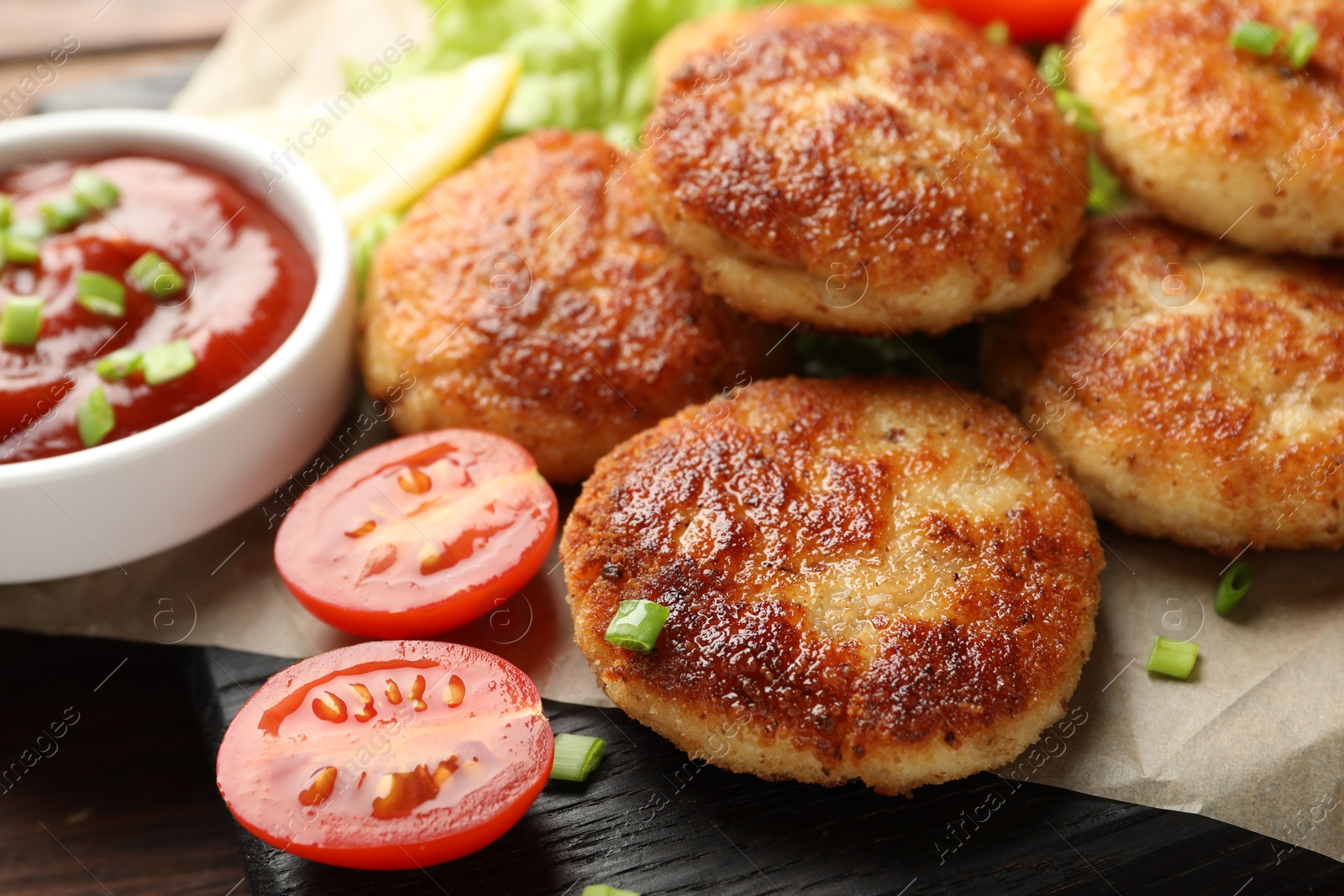 Photo of Delicious patties with green onions, tomato and ketchup on table, closeup