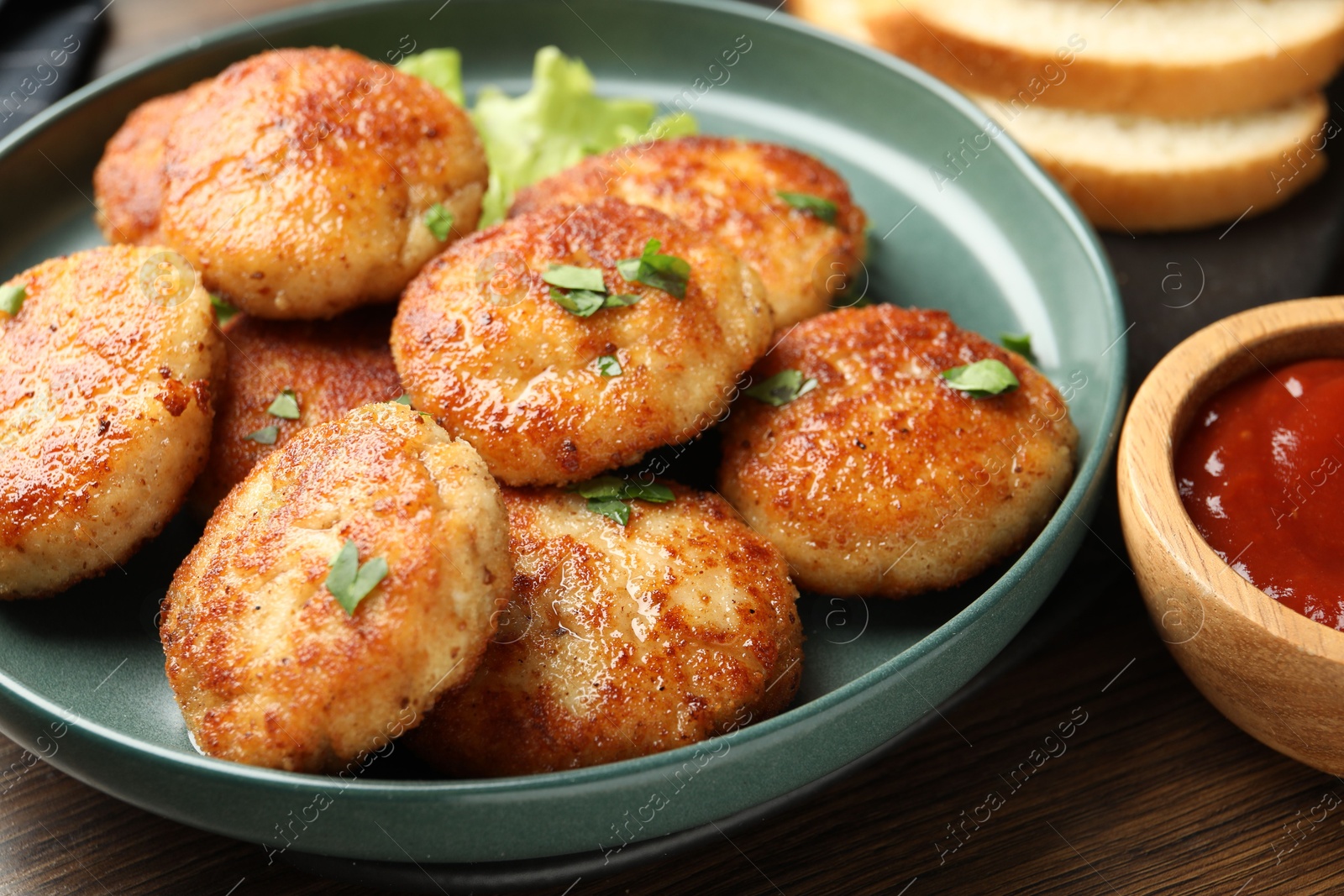 Photo of Delicious patties, parsley and ketchup on wooden table, closeup