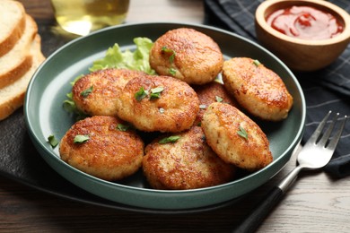 Photo of Delicious patties, parsley, lettuce, ketchup and fork on wooden table, closeup