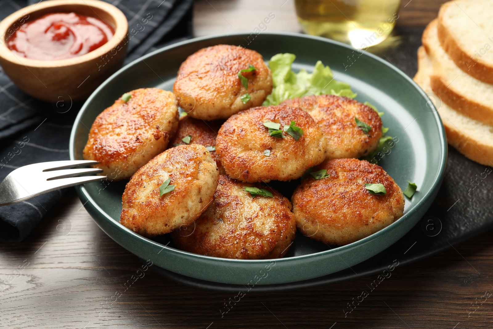 Photo of Delicious patties, parsley, lettuce, ketchup and fork on wooden table, closeup