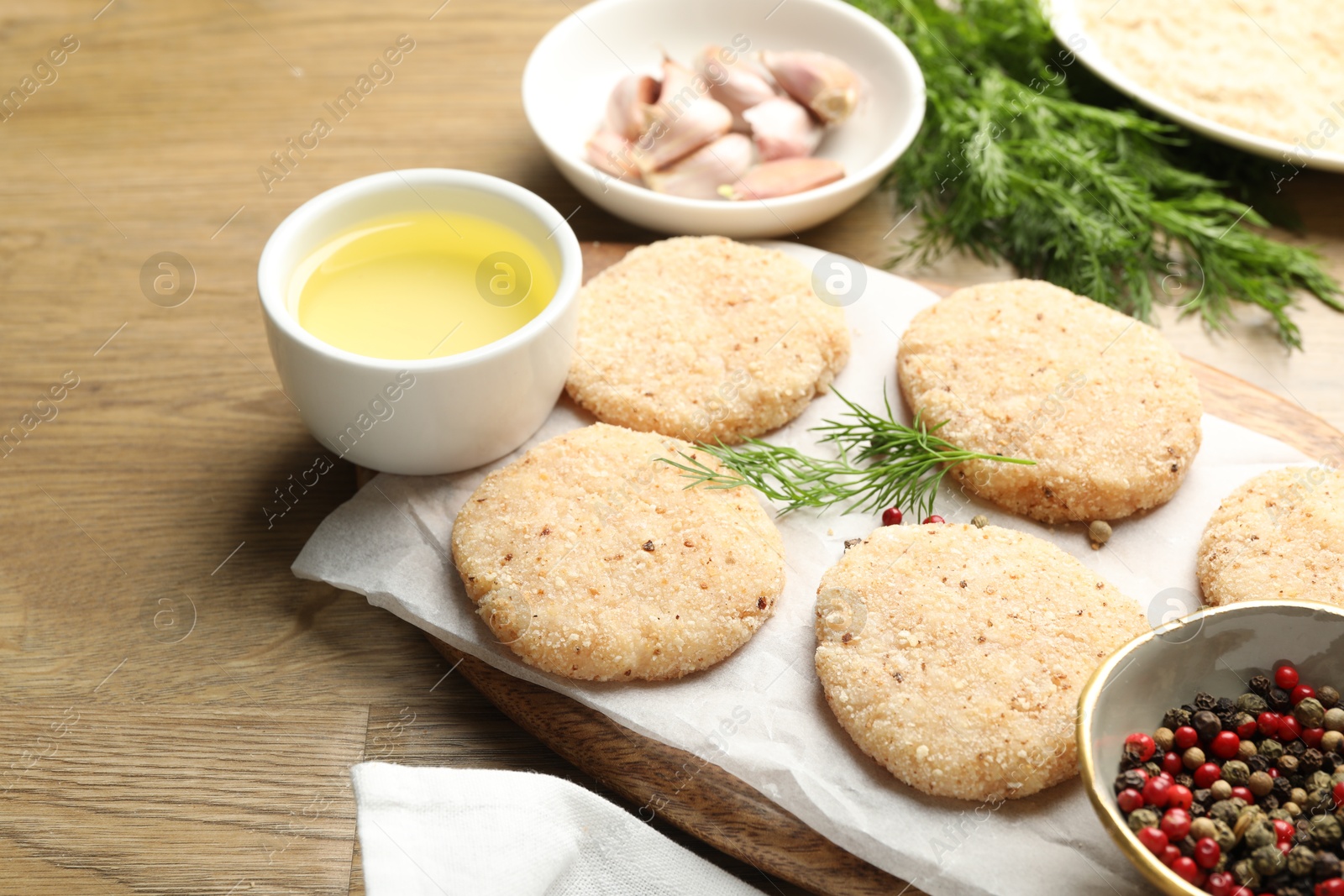 Photo of Many uncooked patties and spices on wooden table, closeup