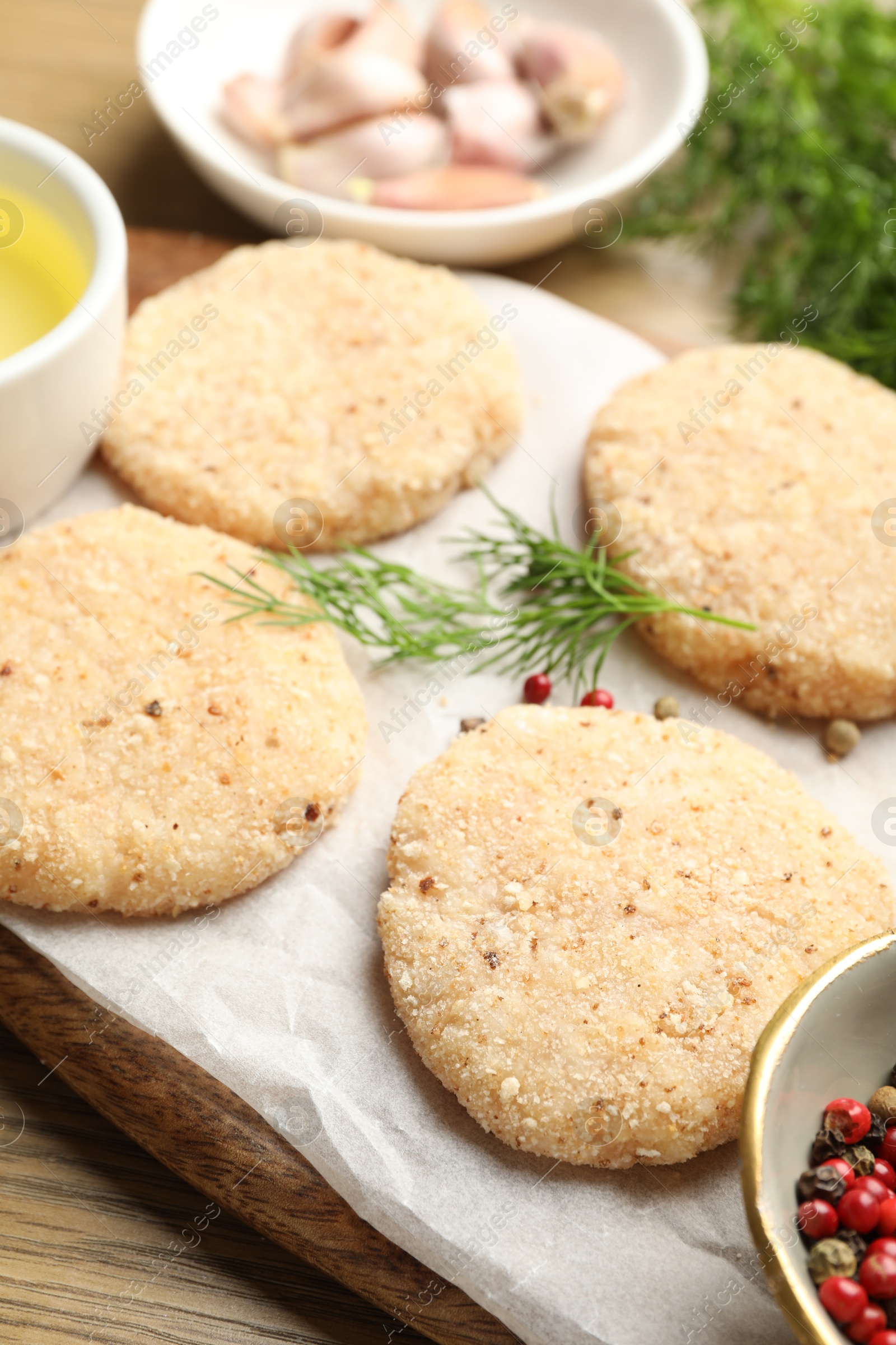 Photo of Many uncooked patties and spices on wooden table, closeup