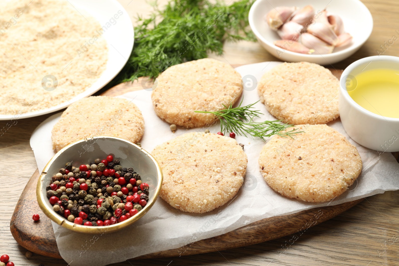 Photo of Many uncooked patties and spices on wooden table, closeup