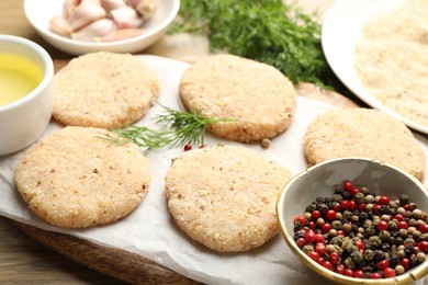 Photo of Many uncooked patties and spices on wooden table, closeup