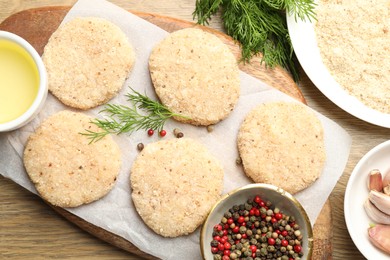 Photo of Many uncooked patties and spices on wooden table, flat lay