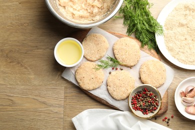 Photo of Many uncooked patties and spices on wooden table, flat lay. Space for text