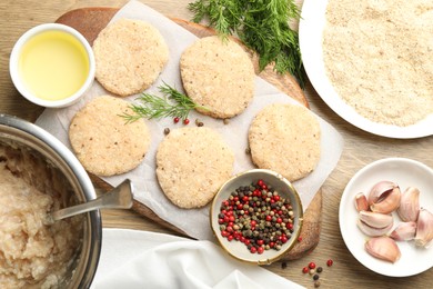 Photo of Many uncooked patties and spices on wooden table, flat lay