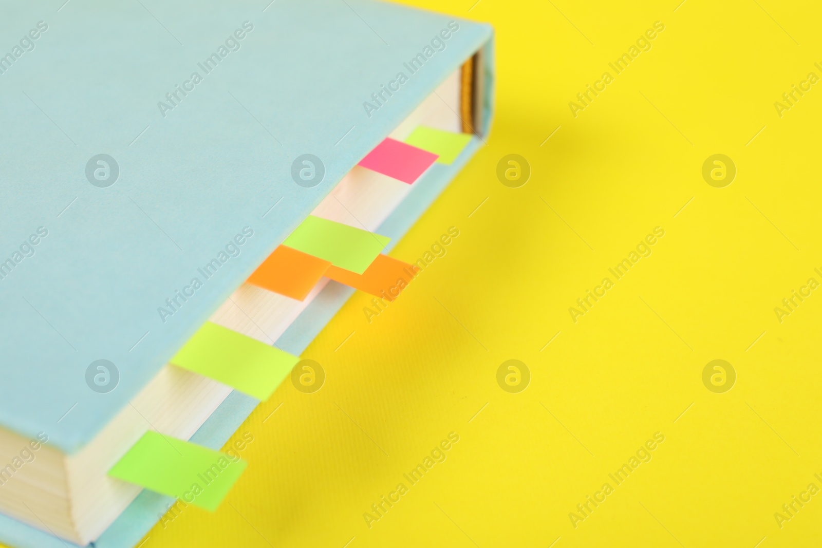 Photo of Book with colorful tabs on yellow background, closeup. Space for text