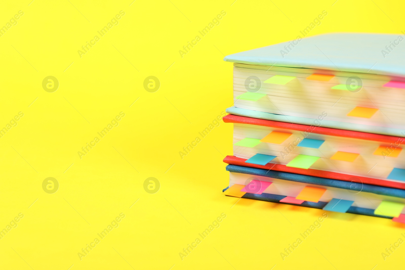 Photo of Books with colorful tabs on yellow background, closeup. Space for text