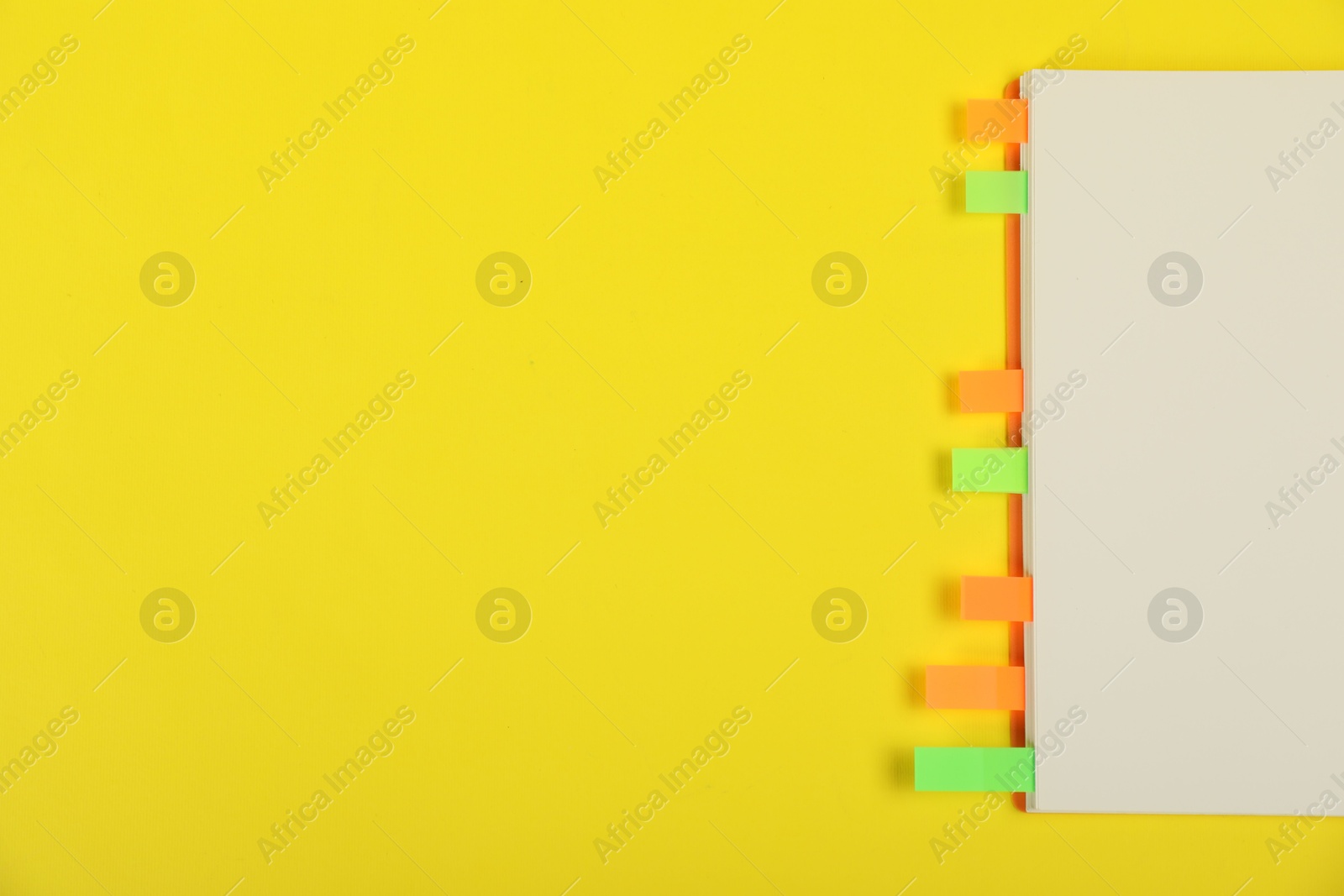 Photo of Book with colorful tabs on yellow background, top view. Space for text