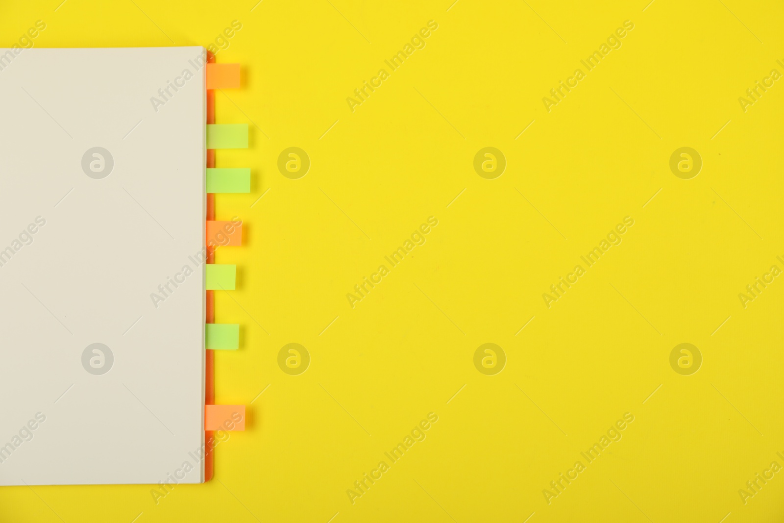 Photo of Book with colorful tabs on yellow background, top view. Space for text