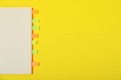 Photo of Book with colorful tabs on yellow background, top view. Space for text