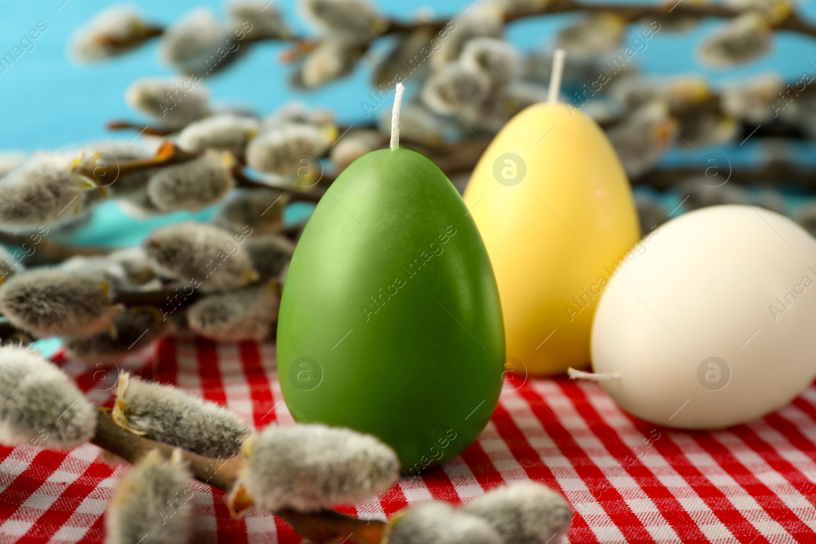 Photo of Colorful egg-shaped candles and willow branches on table, closeup. Easter decor