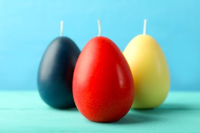 Photo of Colorful egg-shaped candles on turquoise wooden table against light blue background, closeup. Easter decor