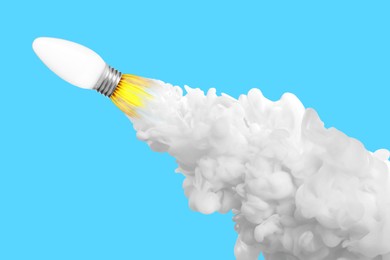 Image of Light bulb flying like rocket with smoke and fire on light blue background. Concepts of idea, startup, creativity, fast success