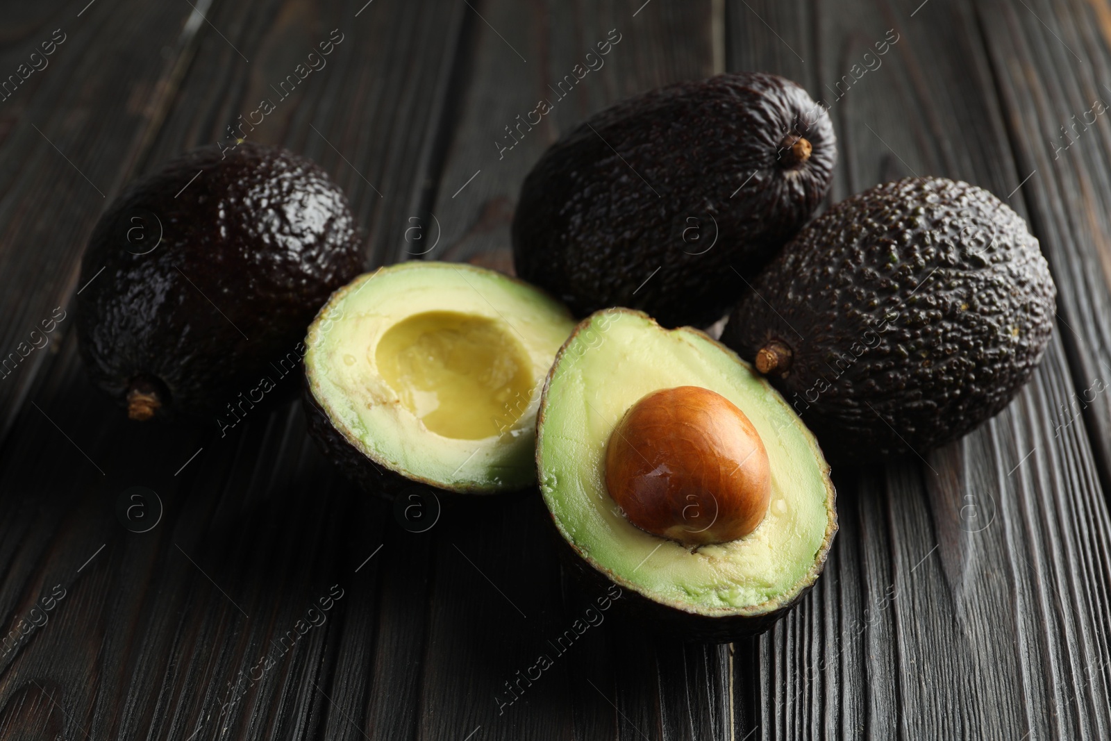 Photo of Whole and cut avocados on dark wooden table, closeup