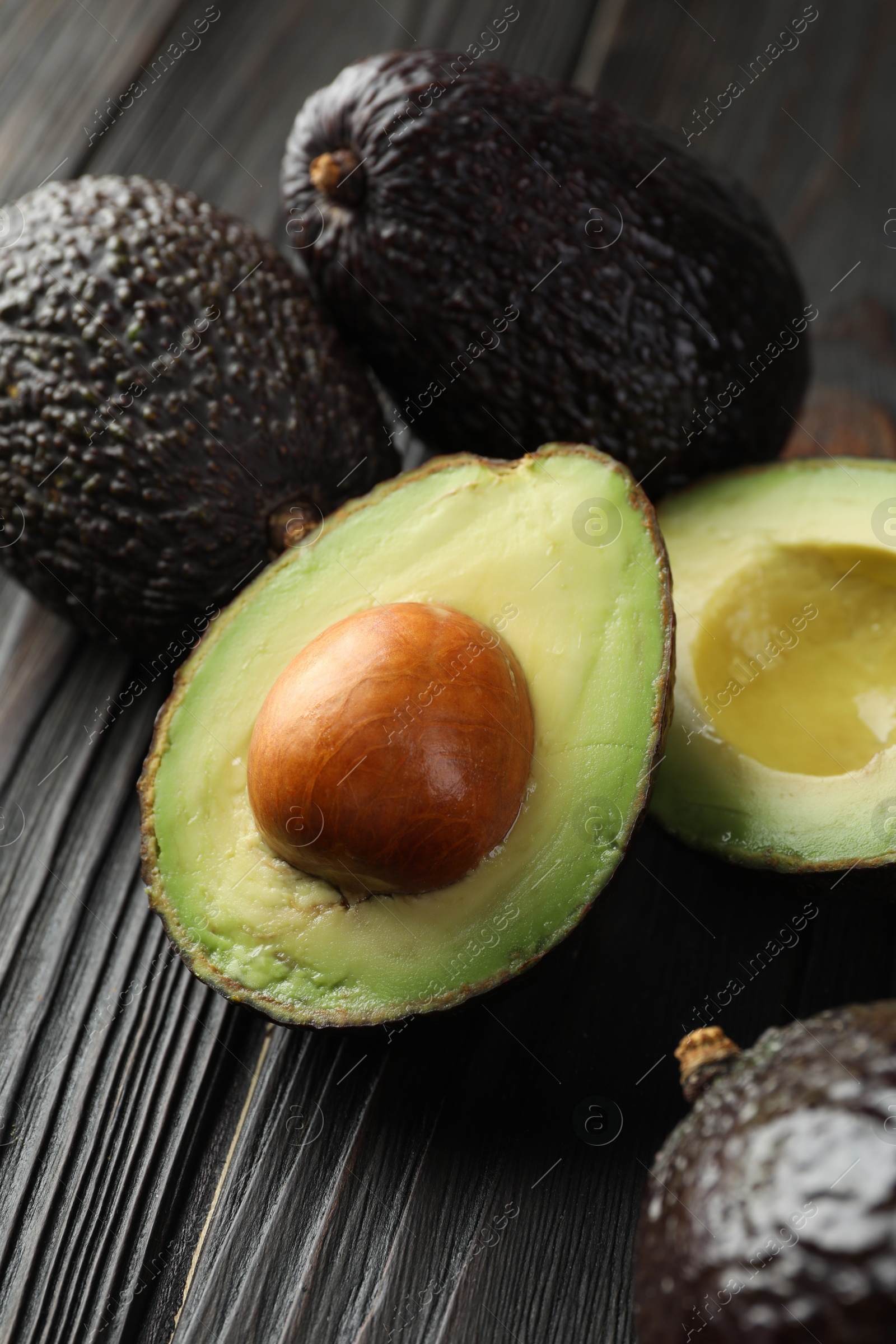 Photo of Whole and cut avocados on dark wooden table, closeup