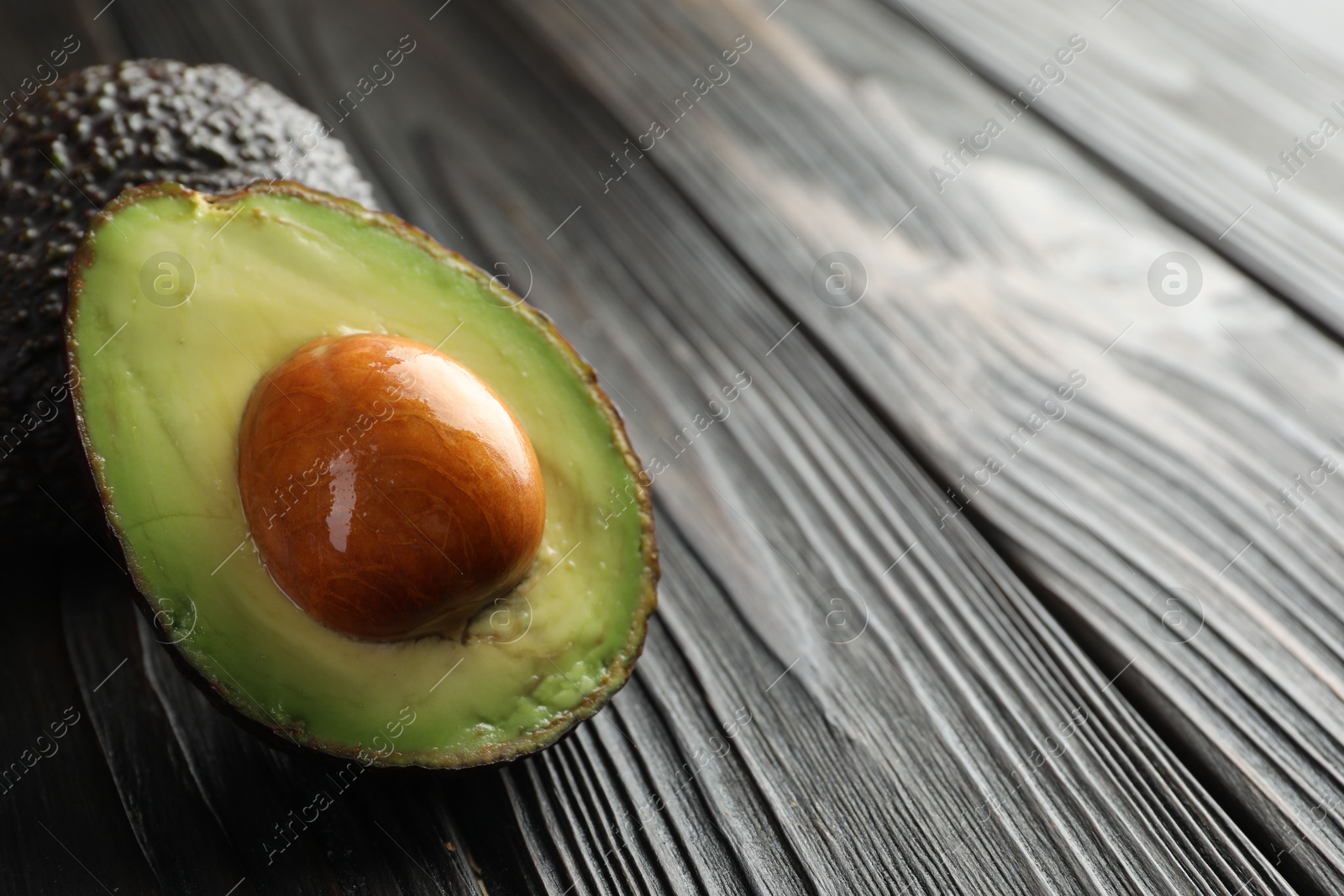 Photo of Whole and cut avocados on dark wooden table, closeup. Space for text