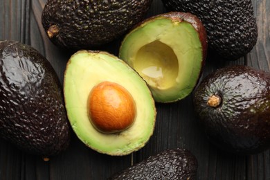 Photo of Whole and cut avocados on dark wooden table, flat lay