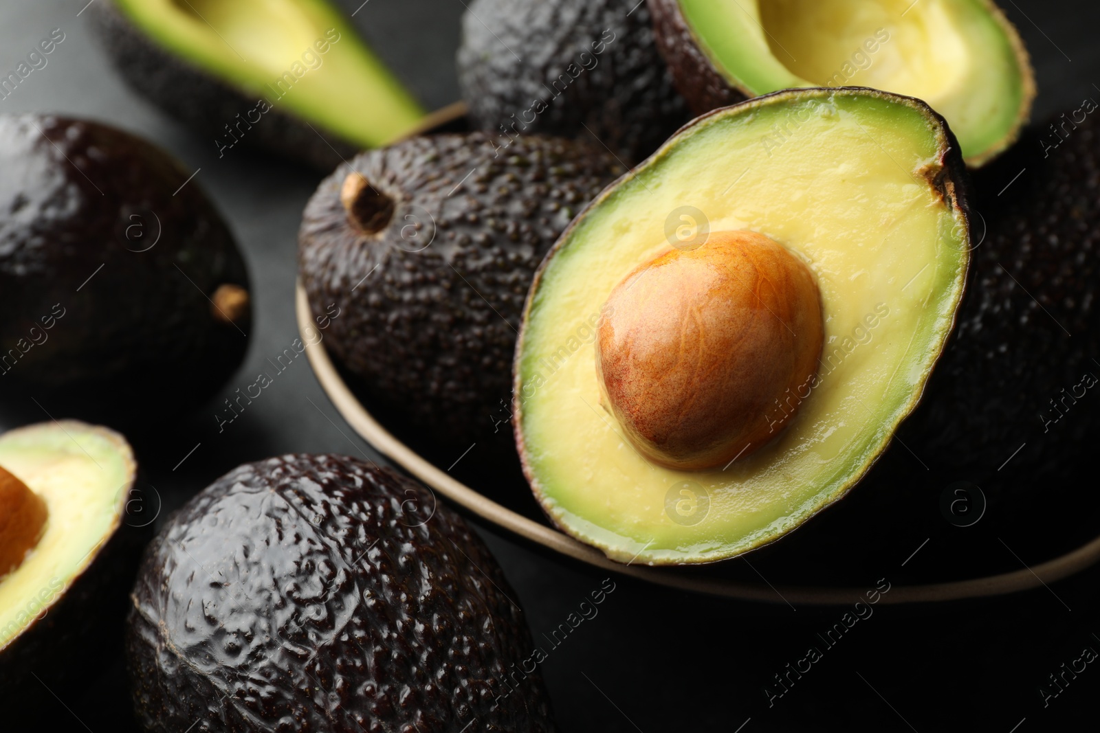 Photo of Whole and cut avocados on dark table, closeup