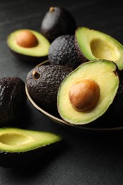 Photo of Whole and cut avocados on dark textured table, closeup