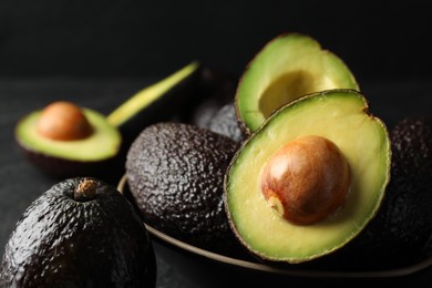 Photo of Whole and cut avocados on dark table against black background, closeup