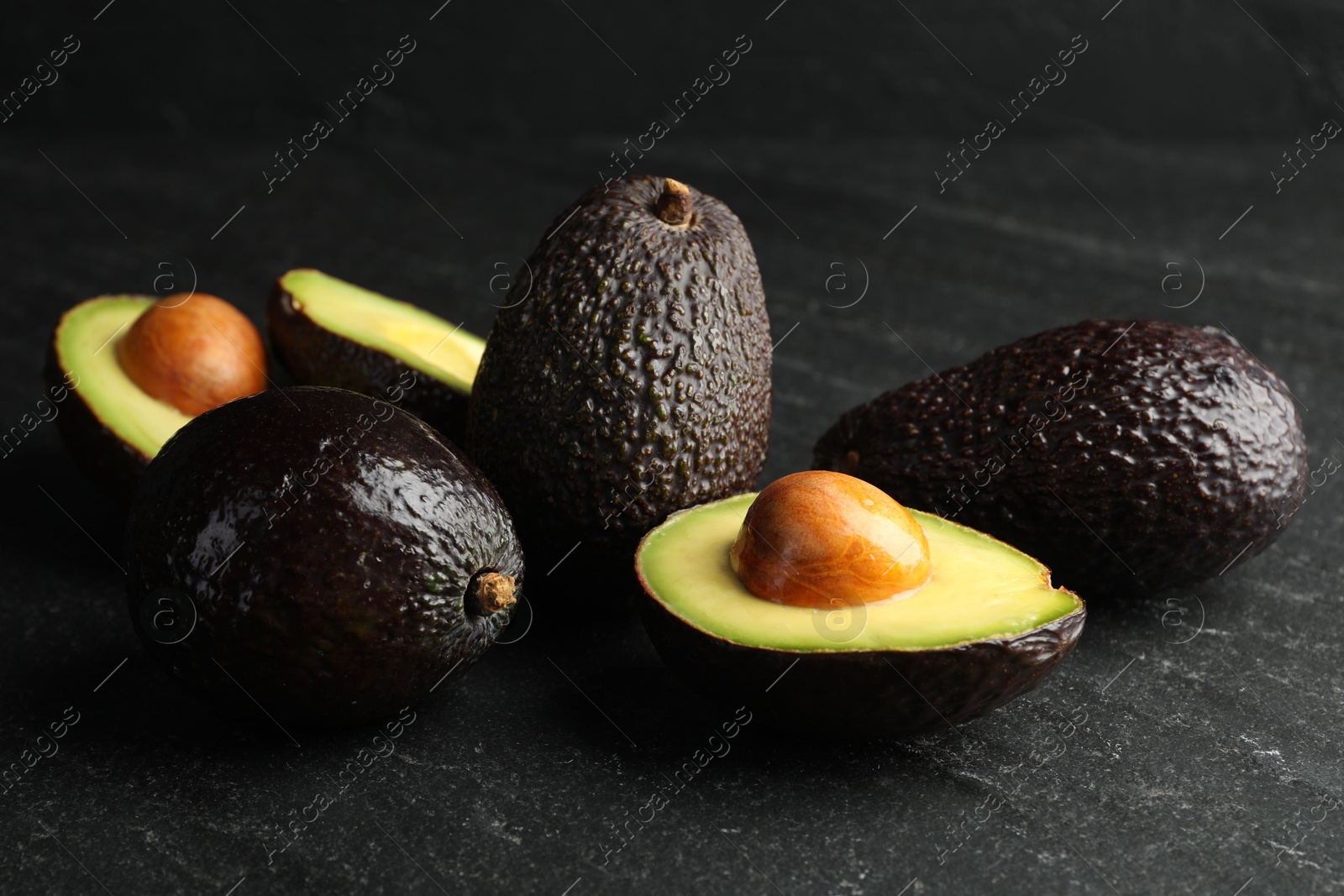 Photo of Whole and cut avocados on dark textured table, closeup