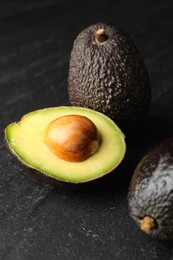 Photo of Whole and cut avocados on dark textured table, closeup