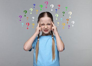 Image of Little girl thinking hard surrounded by question marks on grey background