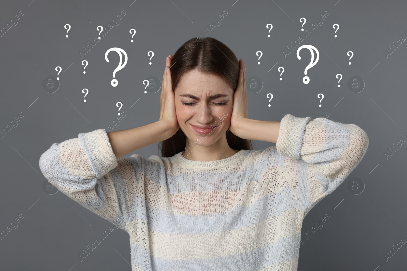 Image of Confused young woman pressing hands to head on grey background. White question marks near her