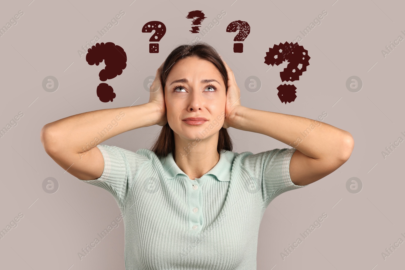 Image of Confused woman pressing hands to head on dark beige background. Question marks near her