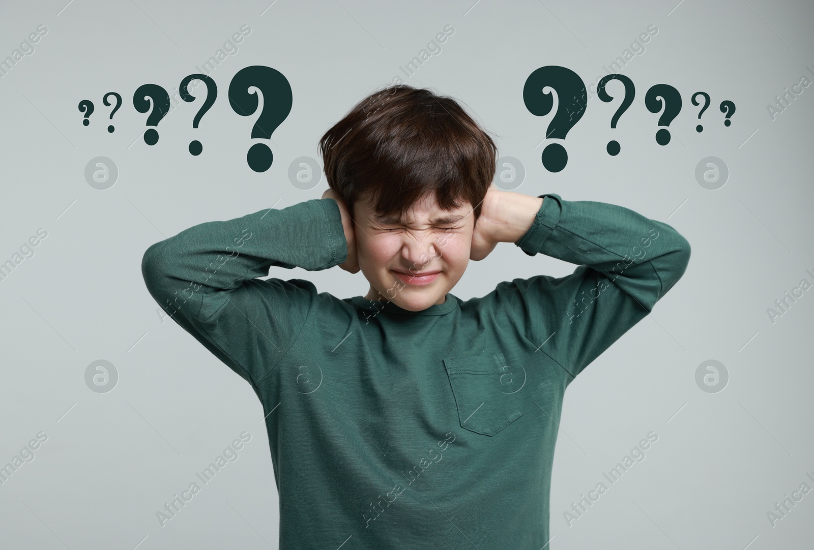 Image of Confused little boy pressing hands to head on grey background. Question marks near child