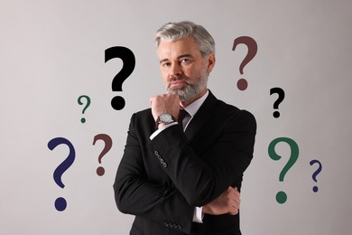 Image of Thoughtful businessman on grey background. Question marks around him