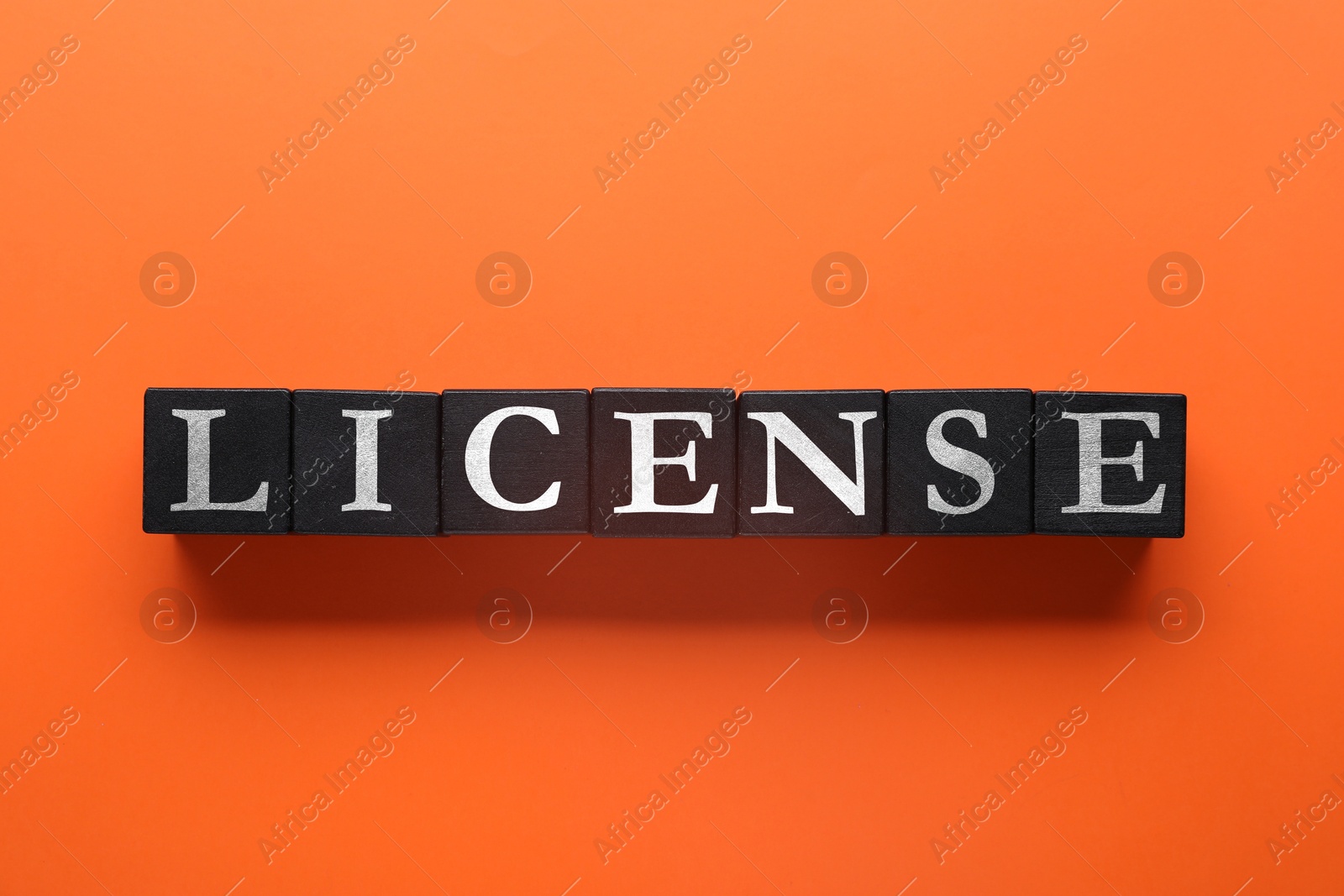 Image of License word made of black cubes with letters on dark orange background, top view