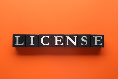 Image of License word made of black cubes with letters on dark orange background, top view