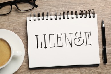 Image of License word written in notebook, coffee, eyeglasses and pen on wooden table, top view