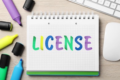 Image of License word written in notebook, markers, computer keyboard and mouse on wooden table, top view